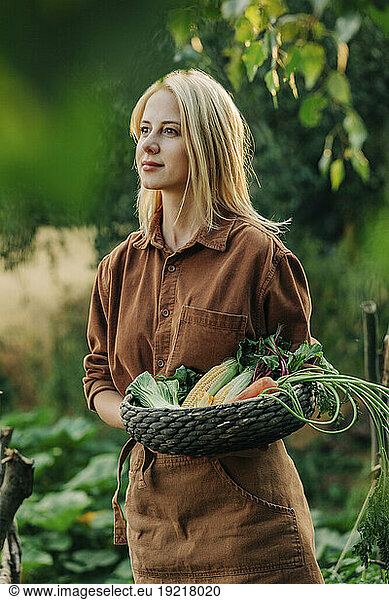 Contemplative woman holding vegetable basket in garden