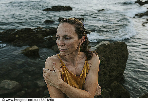 Contemplative woman hugging self at sea shore