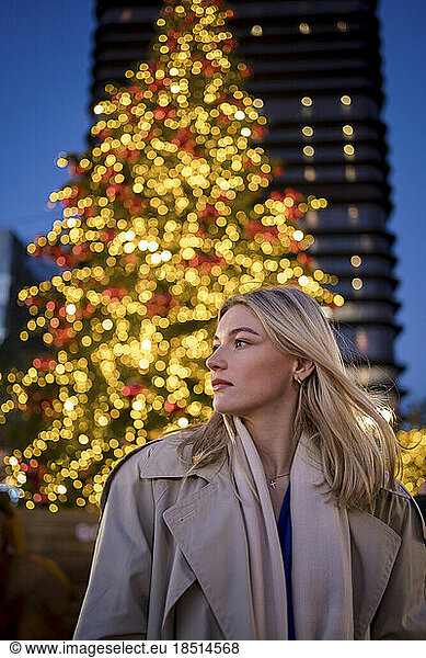 Contemplative woman in front of illuminated Christmas tree at night