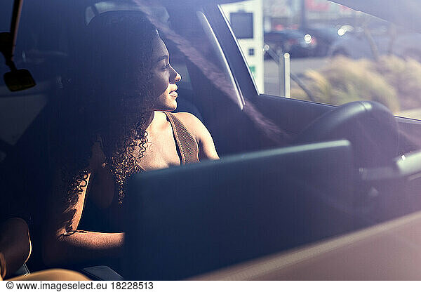 Contemplative woman sitting in electric car seen through windshield