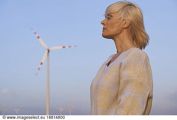 Contemplative woman standing near wind turbine in desert