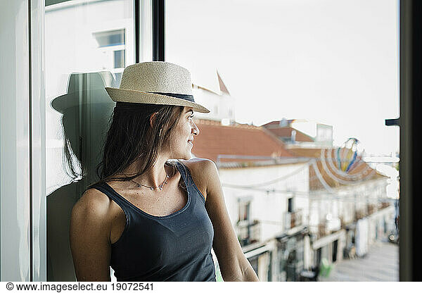 Contemplative woman wearing hat looking through window