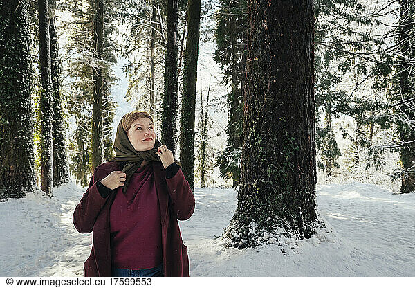 Contemplative woman wearing scarf standing in winter forest