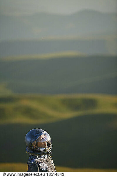 Contemplative woman wearing space helmet in front of landscape