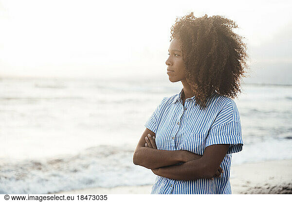 Contemplative woman with curly hair standing in front of sea