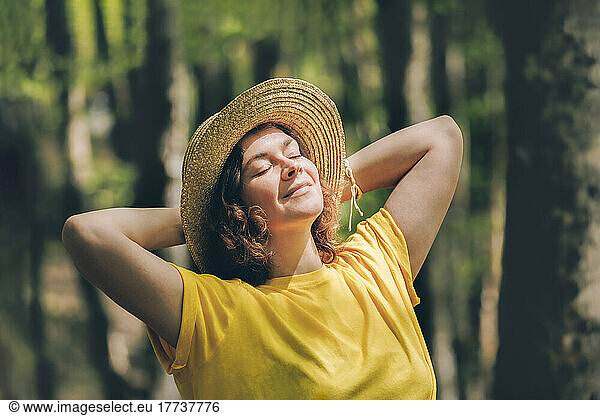 Contemplative woman with hands behind head relaxing in forest