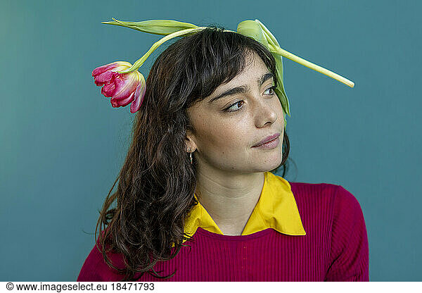 Contemplative woman with tulip on head against green background