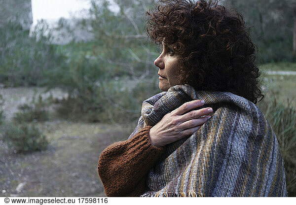 Contemplative woman wrapped in shawl at forest