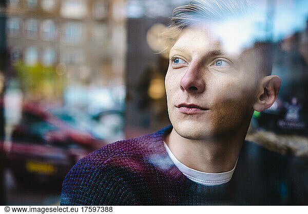 Contemplative young man seen through glass window