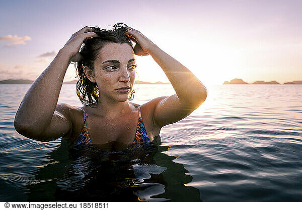 Contemplative young woman with hand in hair in water at sunset