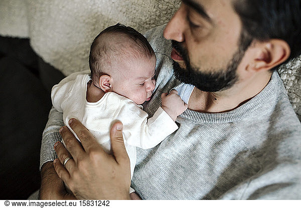 Content early-30â€™s dad with beard holding sleeping newborn