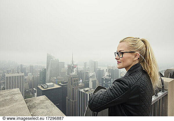 Content woman admiring misty urban city from rooftop