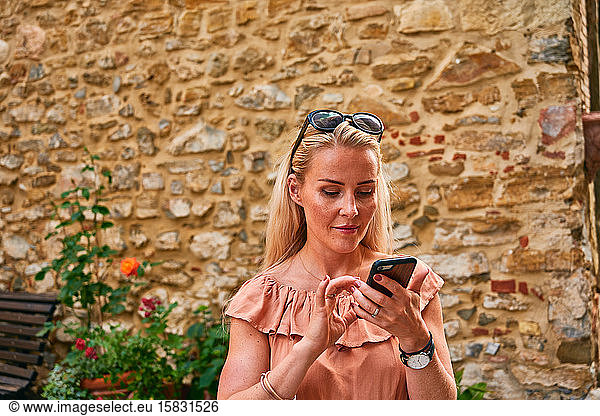 Content woman surfing mobile in old town in Tuscany