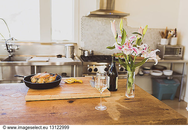 Cooked chicken meat in cooking pan on cutting board with wineglass and vase at table