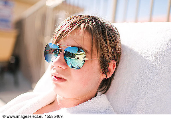 Cool teenage boy wearing mirror image sunglasses on sun lounger at hotel poolside  head and shoulders  Las Vegas  Nevada  USA