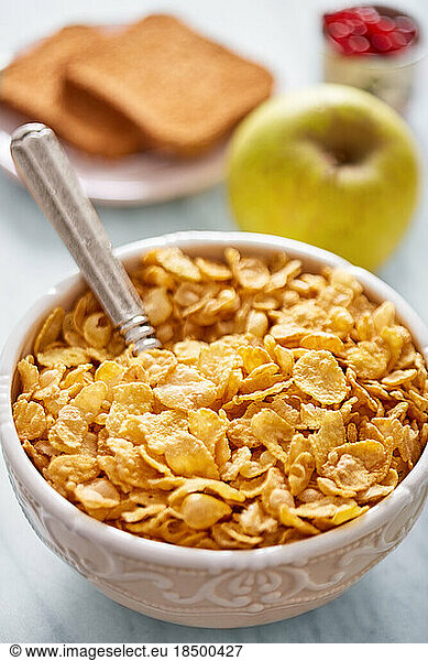 Cornflakes bowl  apple and bread in the background. Breakfast concept