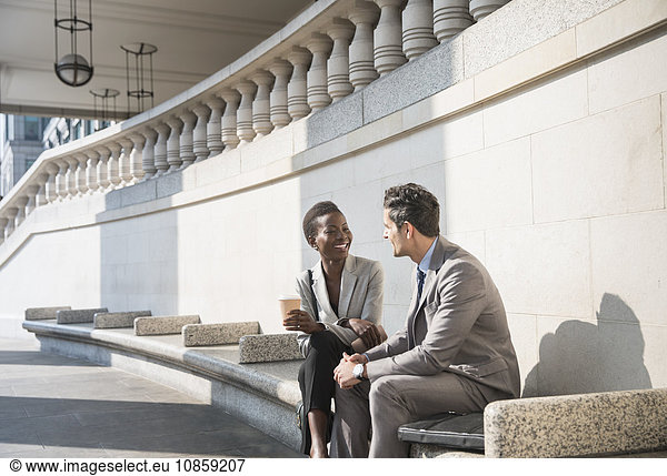 Corporate businessman and businesswoman enjoying coffee break on sunny stairs