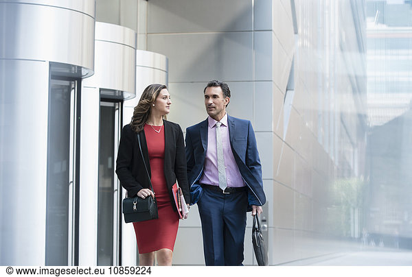 Corporate businessman and businesswoman walking and talking outside building