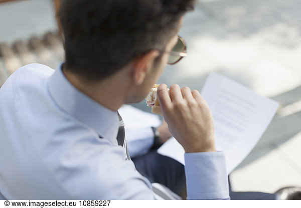Corporate businessman eating lunch and reading paperwork