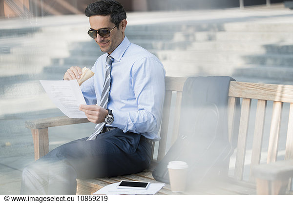 Corporate businessman eating lunch and working on bench