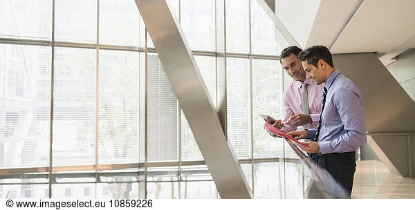Corporate businessmen using digital tablet at railing in office