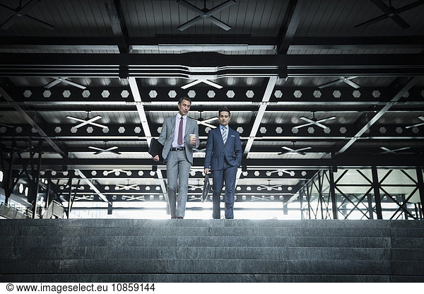 Corporate businessmen with coffee descending modern stairs