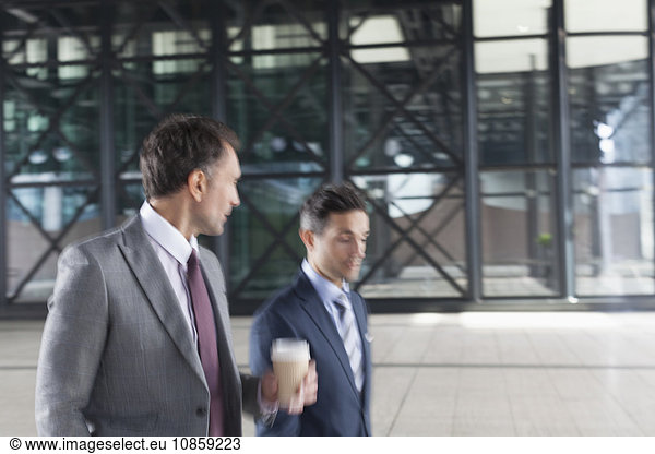 Corporate businessmen with coffee walking and talking outside building