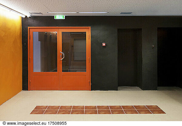 Corridor with orange entrance doors  orange and black colour scheme  tiled floor pattern  public building.