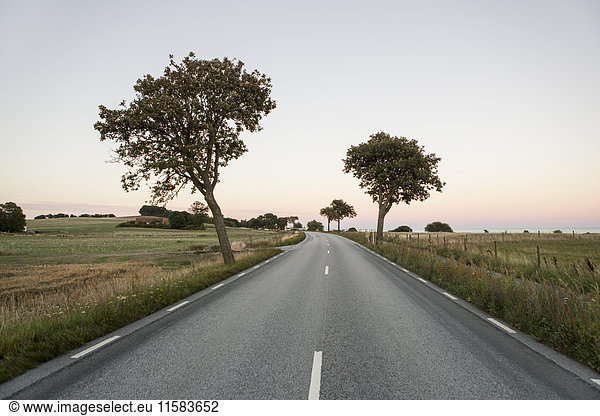 Country road amidst grassy field against clear sky during sunset