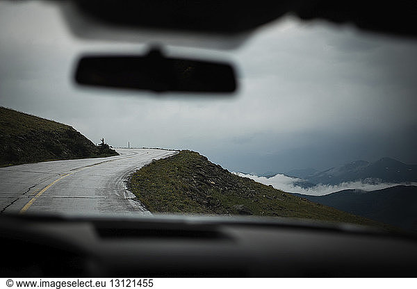 Country road by clouds covered mountains seen through car windshield