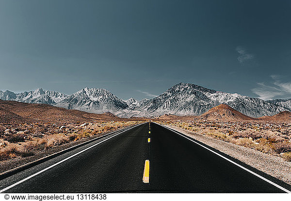 Country road leading towards mountains against blue sky