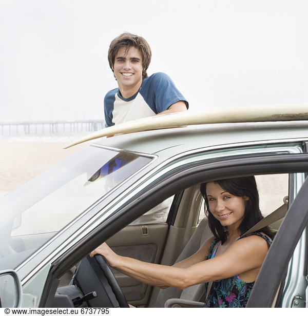 Couple and car with surfboard on top at beach