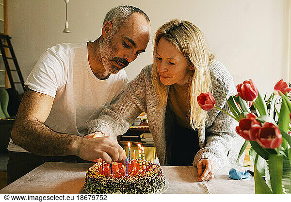 Couple arranging candles on birthday cake together at home