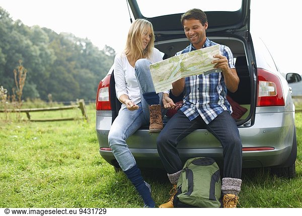 Couple at rear of car map reading preparing for walk