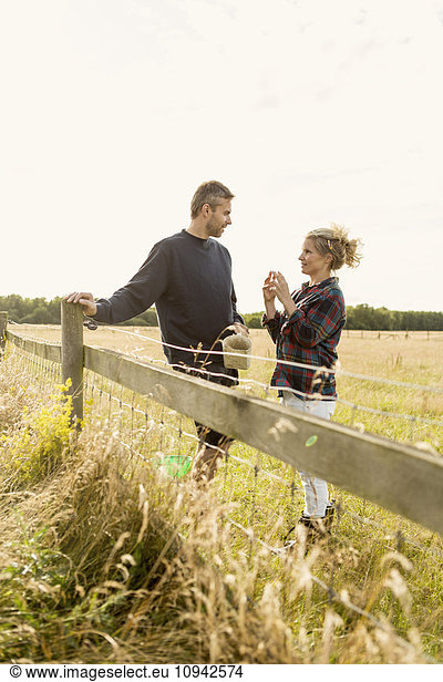 Couple communicating while standing on grassy landscape at farm