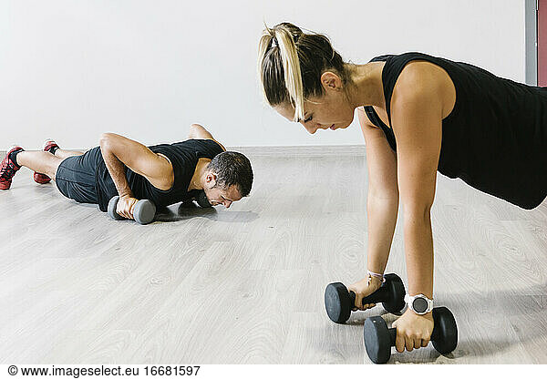Couple doing dumbbell press ups in gym