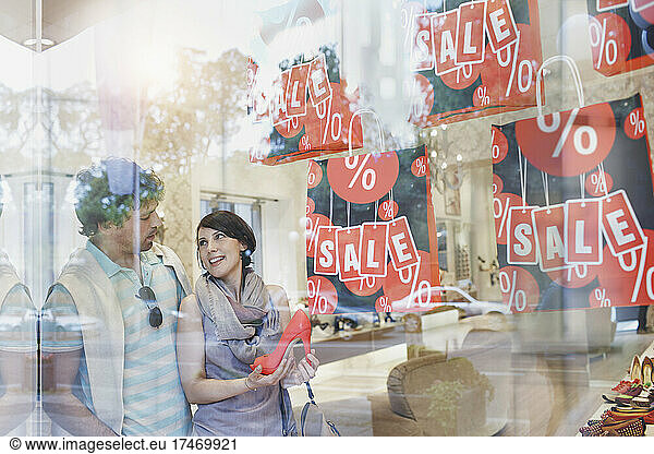 Couple doing shopping in shoe store seen through glass
