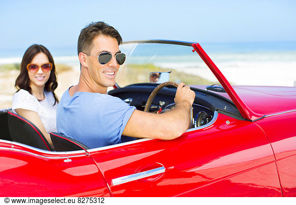 Couple driving convertible on beach