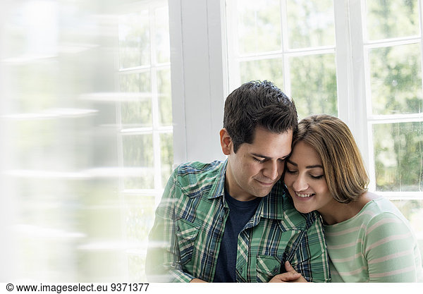 Couple embracing by a window.