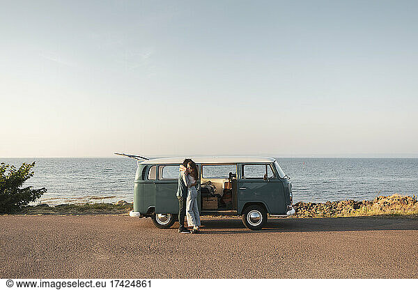Couple embracing by van on road at sea during summer vacation