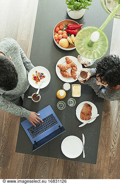 Couple enjoying breakfast and working at laptop in morning kitchen