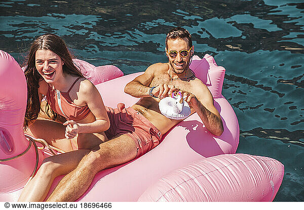 Couple floating on flamingo air mattress in sea at sunny day