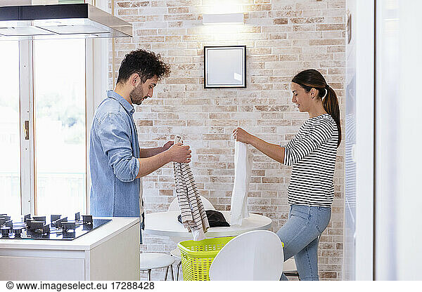 Couple folding clothes together in the kitchen at home