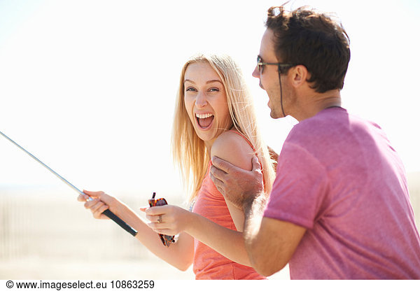 Couple fooling around outdoors  woman holding selfie stick  laughing
