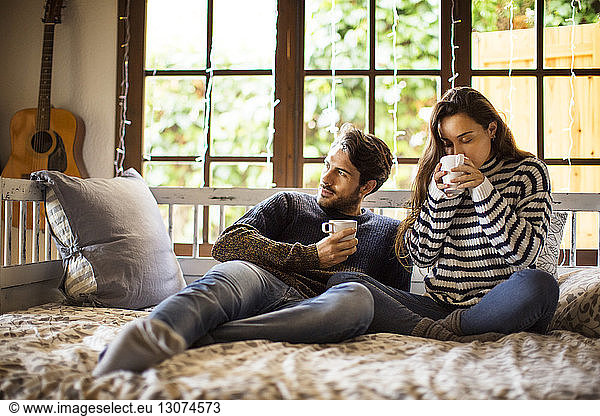 Couple having coffee while sitting on alcove window seat at home