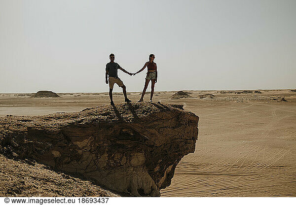 Couple holding hands and standing on rock in desert