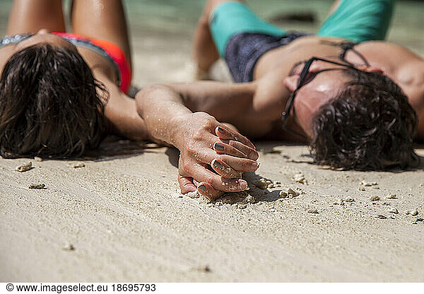 Couple holding hands lying on sand at beach