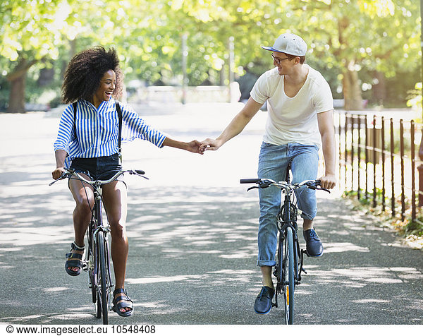 Couple holding hands riding bicycles in urban park