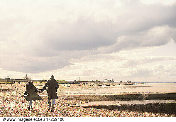 Couple holding hands walking on sunny tranquil winter beach