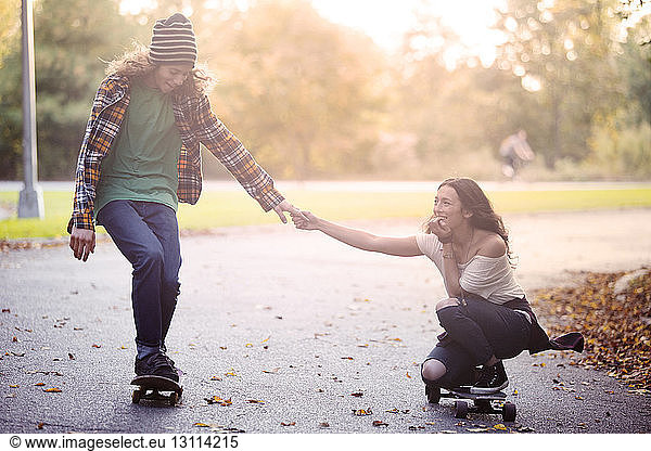 Couple holding hands while skateboarding on street